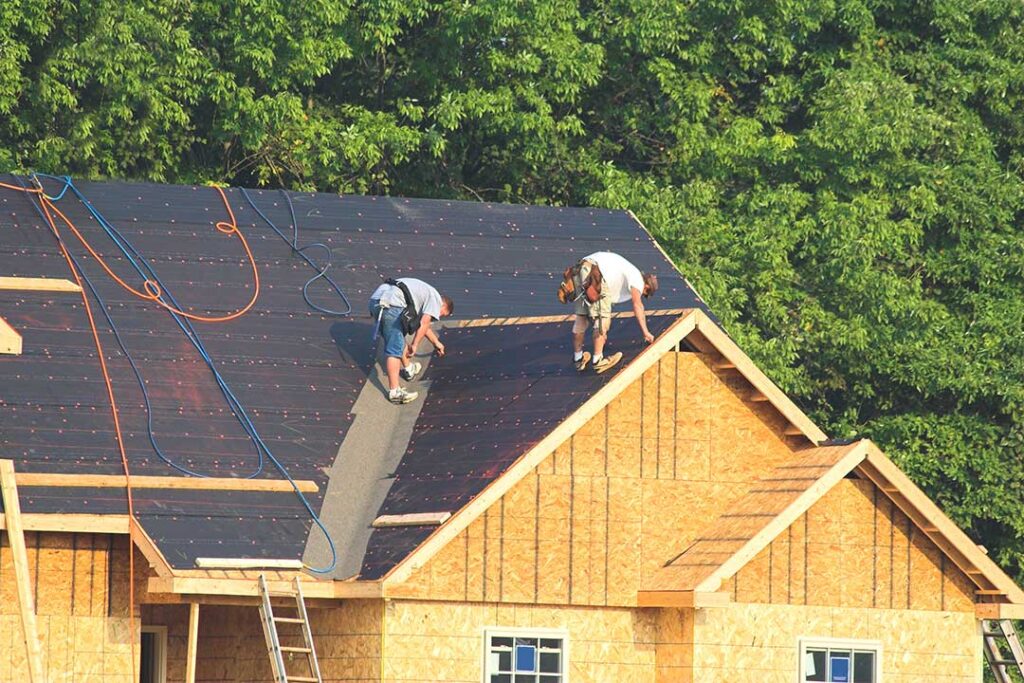 Person using a telescoping soft brush to remove leaves from a roof while standing safely on the ground.